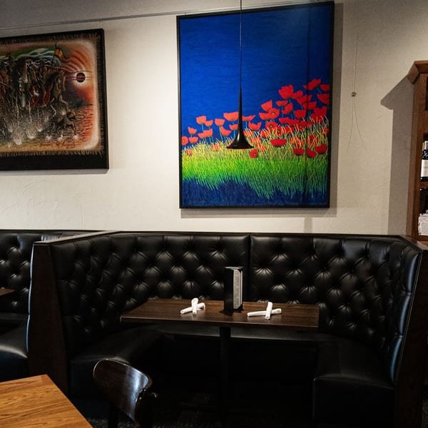 A cozy booth at SamB's Restaurant with dark leather seating, a wooden table, and vibrant wall art.