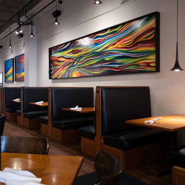 SamB's Restaurant interior with black booths, wooden tables, and colorful abstract art on the walls.
