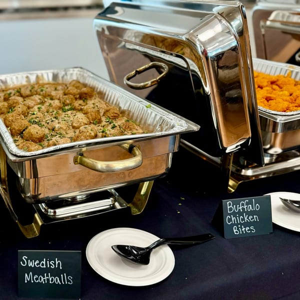 Chafing dishes on a buffet table, with Swedish Meatballs and Buffalo Chicken Bites.