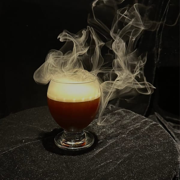 A dark cocktail with a thick layer of foam and dramatic smoke rising from the glass.