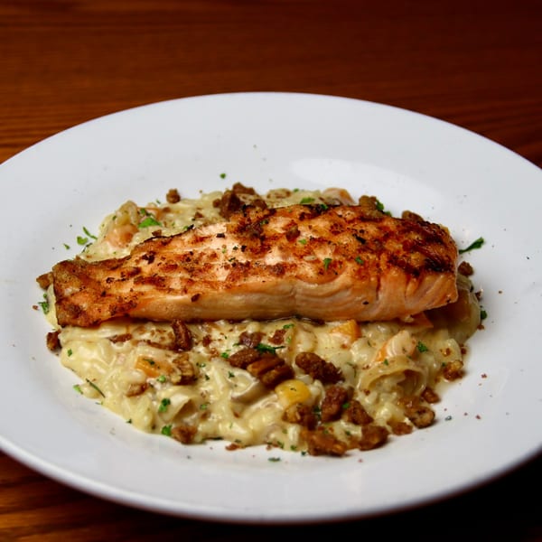 Seared salmon fillet on a bed of creamy pasta with chopped nuts and herbs on a white plate.