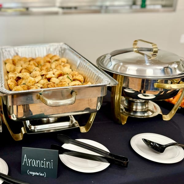 A buffet setup with a chafing dish of vegetarian arancini and another covered chafing dish.